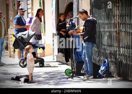 Ein kleines Kind schaut zu einem Straßenbusker auf, der Gitarre spielt, Cadiz, Spanien Stockfoto