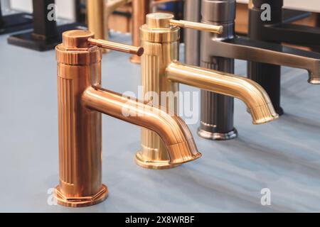Eine Reihe von Gold- und Bronzehähnen ist auf einem Theken ausgestellt. Die Wasserhähne sind in verschiedenen Größen und Stilen, einige davon haben ein moderneres Aussehen und vieles mehr Stockfoto