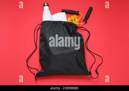 Schwarze Tasche mit Kordelzug, Thermoflasche und Überspringseil auf rotem Hintergrund, flacher Lay Stockfoto
