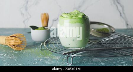 Leckerer Dalgona Matcha Latte im Glas auf dem Tisch Stockfoto