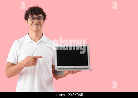 Männlicher Programmierer zeigt auf leeren Laptop auf rosa Hintergrund Stockfoto