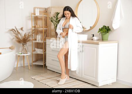 Eine junge Frau massiert ihren Bauch mit einem Holzschaber im Badezimmer Stockfoto