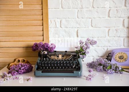 Vintage Schreibmaschine mit Fliederblumen auf dem Tisch im Büro des Autors Stockfoto