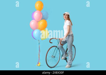 Schöne junge Frau mit Fahrrad und Ballons auf blauem Hintergrund Stockfoto