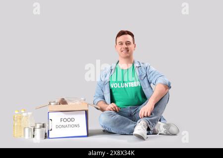 Männlicher Freiwilliger mit Nahrungsspenden auf hellem Hintergrund Stockfoto