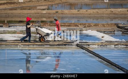 Ein Salzbauern erntet Salz unter der heißen Sommersonne. Dorfbewohner, die auf Salzfarmen in Vietnam arbeiten. Hart arbeitende Männer. Zwei Männer, die sich um Salz kümmern Stockfoto