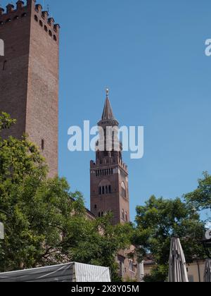 Cremona, Italien - 15. Mai 2024 der majestätische mittelalterliche Backsteinturm erhebt sich in den klaren blauen Himmel, umgeben von grünen Bäumen und einem Kontrast zu einem Vordergrund Stockfoto