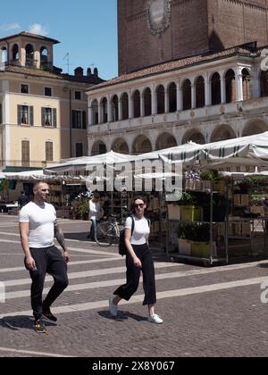 Cremona, Italien - 15. Mai 2024 zwei stilvolle Freunde spazieren an einem sonnigen Tag gemütlich an einem belebten Freiluftmarkt mit historischen Gebäuden und Ständen vorbei Stockfoto