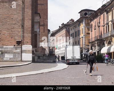 Cremona, Italien - 15. Mai 2024 Personen spazieren mit einem Hund auf einem gemütlichen italienischen Stadtplatz, der von bezaubernden Gebäuden und geschäftigen Aktivitäten des täglichen Lebens gesäumt ist Stockfoto