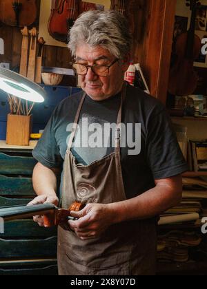 Erfahrener handwerklicher Geigenbauer, der in einer gemütlichen und stimmungsvollen Werkstatt arbeitet. Verwendung traditioneller Handwerkzeuge zur Herstellung und Reparatur von handgefertigten Geigen. Violen Stockfoto