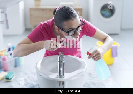 Hygienische Frau: Sie hält ein Waschmittel und kontrolliert Oberflächen mit einer Lupe Stockfoto