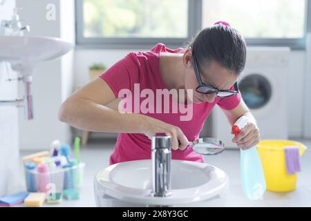 Hygienische Frau: Sie hält ein Waschmittel und kontrolliert Oberflächen mit einer Lupe Stockfoto