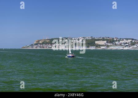 Saint-Adresse mit seinen Gebäuden am Rande des Kieselstrandes und im Vordergrund ein kleines Freizeitsegelboot, das im Ärmelkanal fährt. Stockfoto