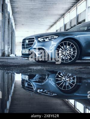 Bulgarien - 05 29 2024: Reflexionen der vorderen Hälfte einer Mercedes S-Klasse in einer Pfütze mit großem leerem Hintergrundgebäude. Stockfoto