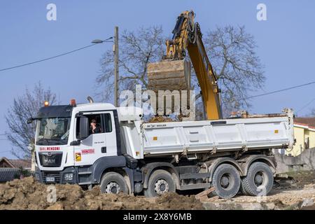 Saint-Max, Frankreich - Blick auf einen weißen Müllwagen MAN TGS 35,420, der von einem Raupenbagger auf einer Baustelle beladen wird. Stockfoto