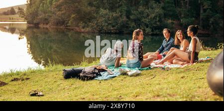 Junge Freunde mit Picknick am Ufer eines Sees. Junge Freunde, einen Tag am See zu genießen. Stockfoto