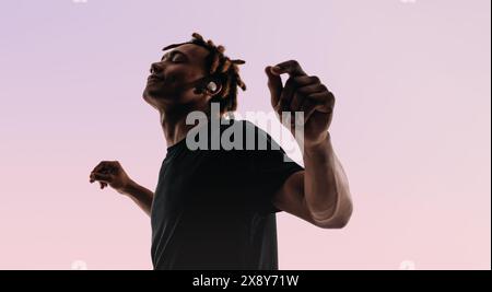 Ein junger Mann mit Dreadlocks tanzt energisch in einem Studio, seine Augen geschlossen und Arme in der Luft ausgestreckt. Ein rosafarbener Hintergrund verleiht seinem s Lebendigkeit Stockfoto