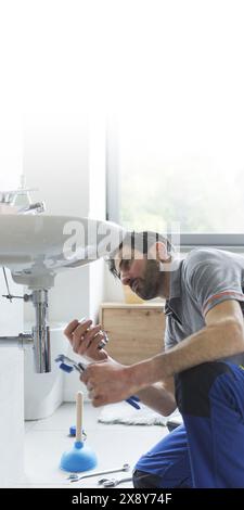 Professioneller Klempner, der an einem Waschbecken im Badezimmer arbeitet und Teile ersetzt Stockfoto