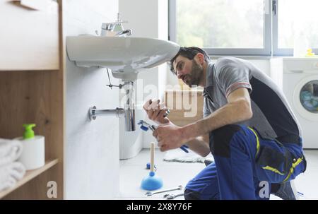 Professioneller Klempner, der an einem Waschbecken im Badezimmer arbeitet und Teile ersetzt Stockfoto