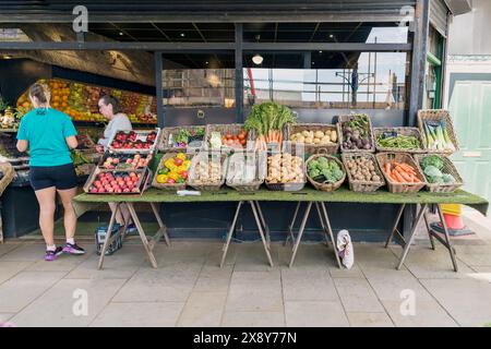 Kunden, die frisches Obst und Gemüse an einem Marktstand im Freien in Großbritannien suchen. Stockfoto