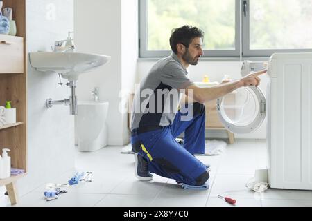 Der Servicetechniker repariert eine Waschmaschine, verwendet das Bedienfeld und überprüft die Einstellungen Stockfoto