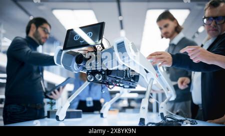 Ein Team von Spezialisten für industrielle Robotik versammelte sich mit einem mobilen Roboter um einen Tisch. Wissenschaftler verwenden Tablet- und Laptop-Computer, um den Automated AI Robotic Dog zu programmieren. Stockfoto