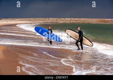 Zwei Surfer mit Surfbrettern gehen aus dem Meer in St Andrews, Fife, Schottland Stockfoto