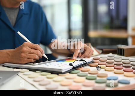 Zugeschnittener Innenarchitekt, der Farbmuster bewertet und ein digitales Tablet am Schreibtisch verwendet Stockfoto