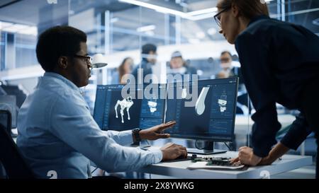 Zwei Industrieingenieure diskutieren über Arbeitsprojekte, sprechen und verwenden Desktop-Computer in der Robotics Startup Facility. Spezialisten und Fachleute, die mobile High-Tech-Roboterhunde erforschen und entwickeln. Stockfoto