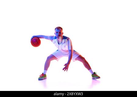 Dynamisches Porträt des jungen Athleten in roter Sportswear-Trainingsdribbeltechnik im Neonlicht vor weißem Studiohintergrund. Stockfoto