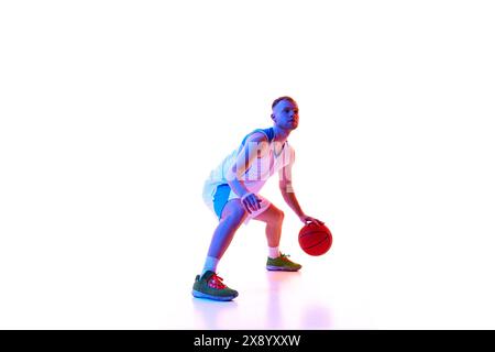 Dynamisches Porträt eines jungen Athleten, Profi-Basketballspielers, der bereit ist, in Neonlicht vor weißem Studiohintergrund Tor zu schießen. Stockfoto