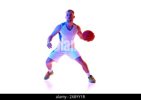 Junger athletischer Mann, professioneller Basketballspieler in roter Uniform, bereit, im Neonlicht vor weißem Studiohintergrund Tor zu schießen. Stockfoto