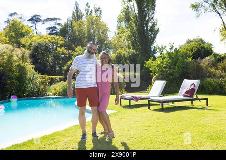 Draußen stehen verschiedene Seniorenfreunde am Pool, beide lächeln Stockfoto