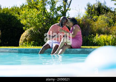 Im Freien genießen verschiedene Seniorenfreunde Drinks am Pool und teilen romantische Momente Stockfoto