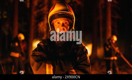 Porträt einer tapferen Feuerwehrfrau, die in professioneller Schutzuniform steht und einen Helm trägt, die Kamera ansieht und posiert. In einem rauchigen Wald während eines Wildlandbrandes stehen. Stockfoto