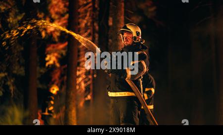 Erfahrener Feuerwehrmann löscht ein Wildlandfeuer tief in einem rauchgefüllten Wald. Profi in Sicherheitsuniform und Helm mit Feuerschlauch zur Bekämpfung von gefährlichem Feuer. Stockfoto