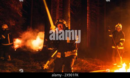 Eine Gruppe erfahrener Feuerwehrleute löscht ein Wildland Brushfire tief im Wald. Professioneller Feuerwehrmann in Sicherheitsuniform und Helm, der Wasser aus dem Feuerschlauch sprüht, um das Wildfeuer zu bekämpfen. Stockfoto