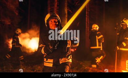 Eine Gruppe erfahrener Feuerwehrleute löscht ein Wildland Brushfire tief im Wald. Professionelle Feuerwehrleute in Sicherheitsuniform und Helm, die Wasser aus dem Feuerschlauch sprühen, um das Wildfeuer zu bekämpfen. Stockfoto