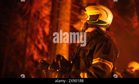 Ein erfahrener Feuerwehrmann löscht ein Wildlandfeuer tief in den Wäldern. Profi in Sicherheitsuniform und Helm, der den Feuerschlauch hält, nach oben blickt, die Windrichtung annimmt und berechnet. Stockfoto