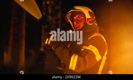 Ein erfahrener Feuerwehrmann löscht ein Wildlandfeuer tief in einem Wald. Professionelles Team in Sicherheitsuniform und Helmen mit Feuerschlauch und Ausrüstung zur Bekämpfung gefährlicher Wildfeuer. Stockfoto