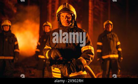 Verschiedene männliche und weibliche Teams professioneller Feuerwehrmänner, die während eines Wildlandfeuers in einem geräucherten Wald stehen, posieren und die Kamera anschauen. Gruppe mit Schutzkleidung, Helmen und Ausrüstung. Stockfoto