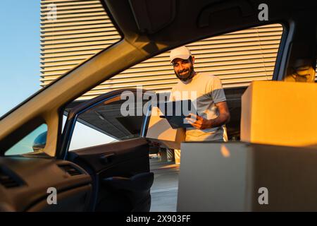 Der Lieferarbeiter entlädt während Sonnenuntergang die Kisten aus dem Auto im Gebäude Stockfoto