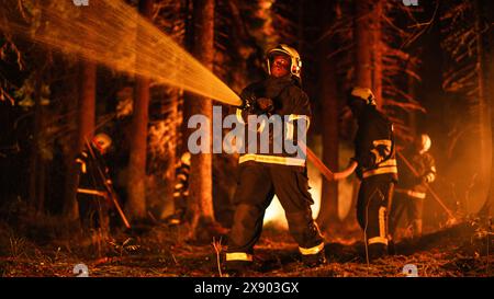 Ein erfahrener afroamerikanischer Feuerwehrmann löscht ein Wildlandfeuer tief in einem Wald. Profi in Sicherheitsuniform und Helm mit einem Feuerwehrschlauch zur Bekämpfung gefährlicher Wildfeuerausbrüche. Stockfoto