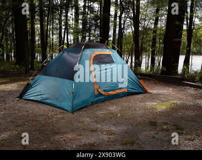 Mit einem blauen Rucksackzelt auf einem Campingplatz, umgeben von Bäumen und einem See dahinter, ist es Zeit, den Outdoor-Lifestyle zu genießen. Stockfoto