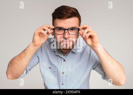 Der junge rothaarige Kerl probiert vor der Kamera eine Brille an Stockfoto