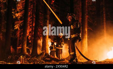 Eine Gruppe erfahrener Feuerwehrleute löscht ein Wildland Brushfire tief im Wald. Professioneller Feuerwehrmann trägt Sicherheitsuniform und sprüht Wasser aus dem Feuerschlauch, um gefährliches Wildfeuer zu bekämpfen. Stockfoto