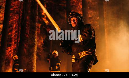 Eine Gruppe erfahrener Feuerwehrleute löscht ein Wildland Brushfire tief im Wald. Professioneller Feuerwehrmann trägt Sicherheitsuniform, sprüht Wasser aus dem Feuerschlauch, um gefährliches Wildfeuer zu bekämpfen. Stockfoto