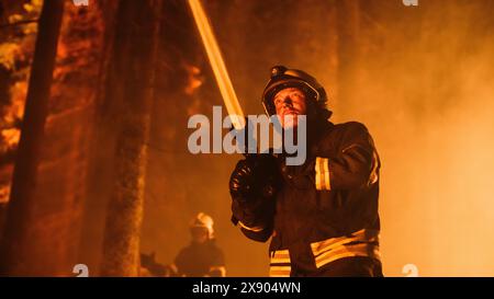 Eine Gruppe erfahrener Feuerwehrleute löscht ein Wildland Brushfire tief im Wald. Professioneller Feuerwehrmann in Sicherheitsuniform und Helm, der Wasser aus dem Feuerschlauch sprüht, um gefährliches Wildfeuer zu bekämpfen. Stockfoto