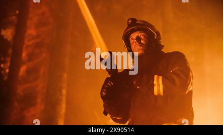 Ein erfahrener Feuerwehrmann löscht ein Wildland Brushfire tief im Wald. Professioneller Feuerwehrmann in Sicherheitsuniform und Helm, der Wasser aus dem Feuerschlauch sprüht, um gefährliches Wildfeuer zu bekämpfen. Stockfoto