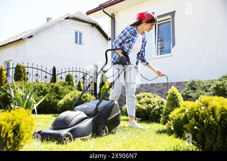 Frau, die grünes Gras mit Rasenmäher im Garten schneidet Stockfoto